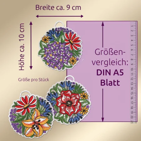 Drei kreisförmig gestickte Blumenornamente mit einer Höhe von ca. 10 cm und einer Breite von ca. 9 cm sind neben einem DIN-A5-Blatt abgebildet, das als Maßstab dient. Die Ornamente zeigen bunte Blumen und Blätter auf einem neutralen Hintergrund. Ein Lineal zeigt die Maße in Zentimetern an.