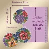 Drei kreisförmig gestickte Blumenornamente mit einer Höhe von ca. 10 cm und einer Breite von ca. 9 cm sind neben einem DIN-A5-Blatt abgebildet, das als Maßstab dient. Die Ornamente zeigen bunte Blumen und Blätter auf einem neutralen Hintergrund. Ein Lineal zeigt die Maße in Zentimetern an.