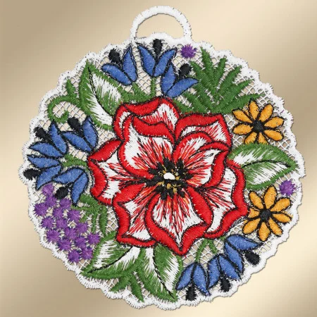 Ein rundes besticktes Spitzendeckchen zeigt in der Mitte eine rot-weiße Blüte, die von blauen, gelben und violetten Blüten mit grünen Blättern umgeben ist. Das Deckchen ist mit einer weißen Spitzenkante mit Wellenschliff versehen. Am oberen Ende ist eine kleine Schlaufe zum Aufhängen angebracht.