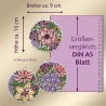 Drei runde, gestickte Ornamente mit unterschiedlichen, farbenfrohen Blumenmustern sind abgebildet. Der deutsche Text gibt an, dass jedes Ornament etwa 10 cm hoch und 9 cm breit ist. Ein Vergleich im Format DIN A5 verwendet ein violettes Lineal und einen schattierten Kasten im Hintergrund.