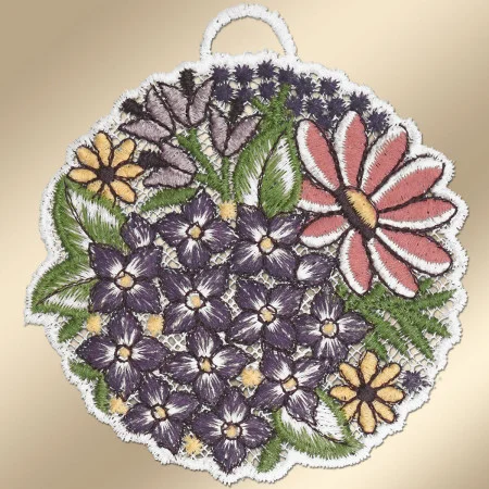Ein kreisförmiger gestickter Aufnäher zeigt violette, gelbe und rosa Blumen mit grünen Blättern. Er ist mit weißer Spitze eingefasst und hat oben eine kleine Schleife. Der Hintergrund ist in zartem Beige gehalten, und die Blumenstickerei enthält detaillierte, mehrfarbige Stiche.