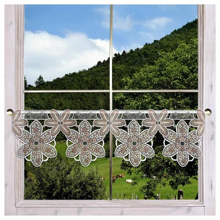 Ein Fenster mit einem hellen Holzrahmen ist mit einem Spitzenvolant mit großen, detaillierten Blumenmustern in Braun und Weiß versehen. Durch das Fenster ist eine grüne Landschaft mit Bäumen, Hügeln und grasenden Kühen unter einem teilweise bewölkten Himmel zu sehen.