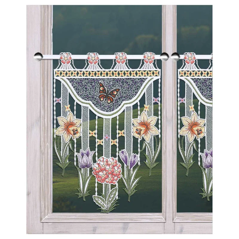 Gardinenpaneel aus Spitze mit mehrfarbiger Blumenstickerei, die Lilien, Krokusse, eine rosa Kugelprimel und einen braunen Schmetterling darstellt. Das Paneel hat gebördelte Ränder und wird oben mit Schlaufen an einer Stange aufgehängt, die ein Fenster mit Blick auf grünes Laub einrahmt.