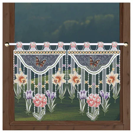 Ein holzgerahmtes Fenster ist mit einem Spitzenvolant mit Blumen- und Schmetterlingsmustern versehen. Der Vorhang zeigt rosa, lila und gelbe Blumen, grüne Blätter und zwei braune Schmetterlinge. Durch das Fenster ist eine Landschaft im Freien zu sehen.