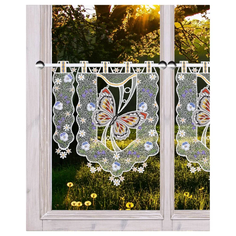 Spitzenvorhänge mit Schmetterlings- und Blumenmustern sind an einem Holzfenster aufgehängt. Das Sonnenlicht fällt durch die Bäume draußen und beleuchtet das grüne Gras und die gelben Blumen auf der anderen Seite des Fensters.