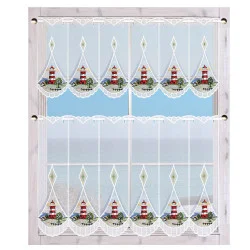 Ein Fenster mit transparenten weißen Spitzenvorhängen, die mit rot-weißen Leuchtturm-Motiven verziert sind. Die Vorhänge sind in einen oberen und einen unteren Teil unterteilt und rahmen den Blick auf die Meereslandschaft und den Himmel ein. Der Fensterrahmen wirkt rustikal und ist hell gefärbt.