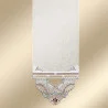 Ein beiges Textil hängt senkrecht herab und weist am unteren Rand ein symmetrisches Stickmuster auf. Die Stickerei zeigt Blumenmotive in Pastellrosa, -blau und -grün mit spitzenartigen Akzenten. Der Hintergrund bildet einen sanften goldenen Farbverlauf.