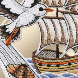 Ein gestickter Aufnäher zeigt eine Möwe mit ausgebreiteten Flügeln, die über einem hölzernen Segelschiff mit weißen Segeln und orangefarbenen Akzenten fliegt, das auf blauen Wellen schwimmt. Der Hintergrund ist beige, und der gesamte Aufnäher weist ein gesticktes, strukturiertes Design auf.