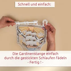 Eine Person fädelt eine Gardinenstange durch die gestickten Schlaufen eines Spitzenvorhangs mit einem Schiffs- und Sonnenmotiv. Der deutsche Text lautet: „Schnell und einfach: Die Gardinenstange einfach durch die gestickten Schlaufen fädeln – fertig!“.