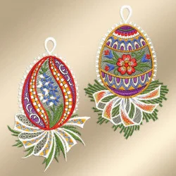 Zwei aufwendig bestickte Ostereier mit bunten Mustern aus Blumen, Blättern und dekorativen Bordüren. Jedes Ei hat oben eine weiße Aufhängeschlaufe und ruht auf einem detailliert grün und weiß bestickten Sockel. Der Hintergrund ist in einem weichen Beigeton gehalten.