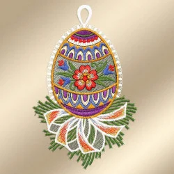 Ein aufwendig besticktes Ornament in Form eines Eies zeigt bunte Muster, eine rote Blume in der Mitte und grünes Laub. Es ist mit Spitze umrandet, mit einer weißen Aufhängeschlaufe versehen und mit einer dekorativen Schleife an der Basis geschmückt, die vor einem weichen beigen Hintergrund steht.