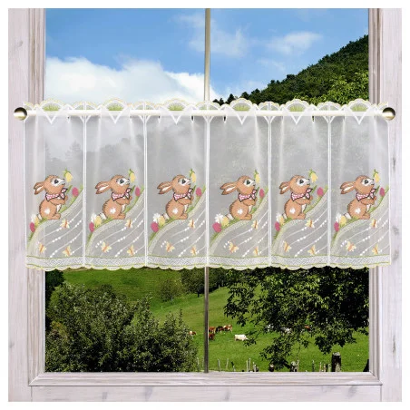 Ein durchsichtiger kurzer Vorhang mit gestickten Häschen und bunten Blumen hängt an einem Fenster. Draußen ein malerischer Blick auf grüne Hügel, Bäume und Küheunter blauem Himmel grasen.